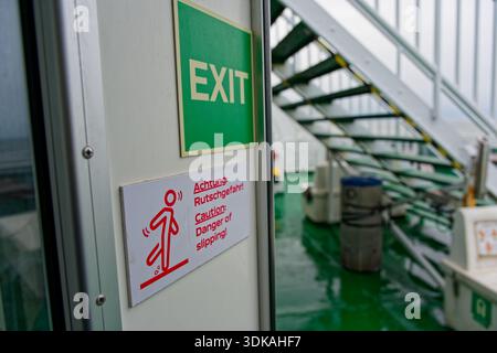 On the ship deck an Exit label sits beside a slipping figure icon, with warnings Achtung Rutschgefahr in german, means Danger of slipping to help prev Stock Photo