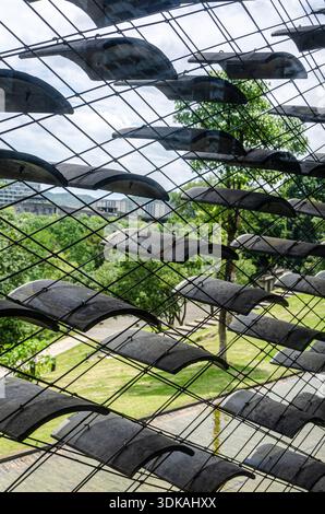 Detailed close up view of traditional curved grey roof tiles hanging on metal wires creating a semi-transparent architectural screen pattern. Stock Photo