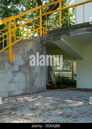 Outdoor architectural detail of grey concrete stairs with bright yellow metal handrails and fallen leaves on the ground. Stock Photo
