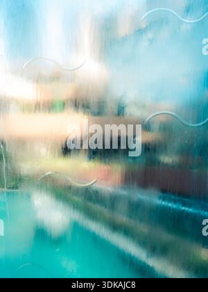 Abstract colorful background view through wet glass with flowing water and wave patterns, creating a beautiful blurred effect. Stock Photo