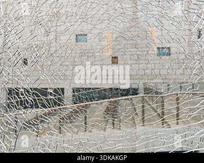 Abstract texture background of broken tempered safety glass with a spiderweb crack pattern, blurring the view of the architecture behind it. Stock Photo