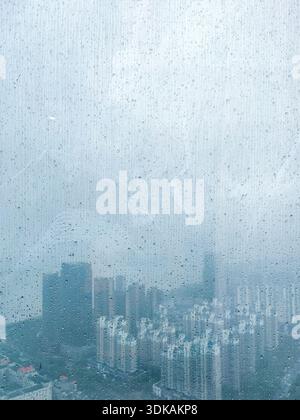 Moody view of modern city skyscrapers and buildings seen through a wet glass window covered in rain drops on a cloudy day. Stock Photo