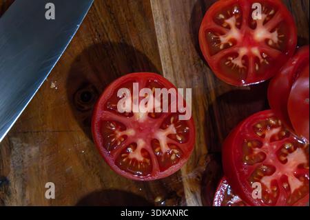 Slices of ripe tomato on a wood cutting board by a knife Stock Photo