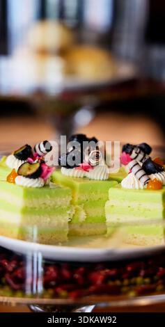 Elegant pistachio sponge cakes featuring fresh blueberries and cream sitting on glass platter. High-end dessert presentation for luxury catering and h Stock Photo