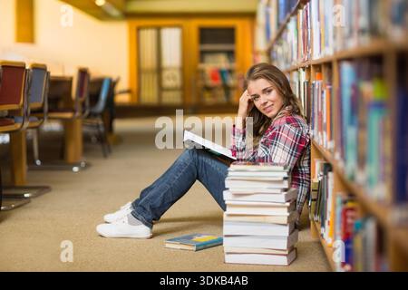 Woman reading open book on library carpet, leaning against shelves, books beside, copy space. Cozy, warm, focus, study, nook, volume, literature Stock Photo