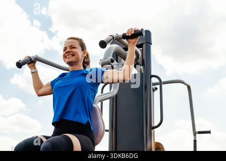 Smiling fit woman exercising in outdoor gym park. Stock Photo