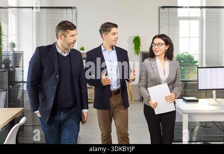 Professional team of three coworkers walking through office discussing strategy Stock Photo