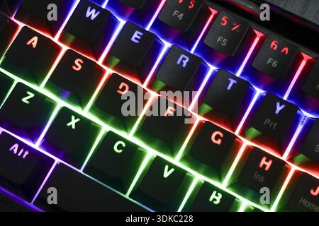 Close up of gaming keyboard with colorful RGB backlit keys. Modern computer technology equipment glows with vibrant neon light in dark room for an exc Stock Photo