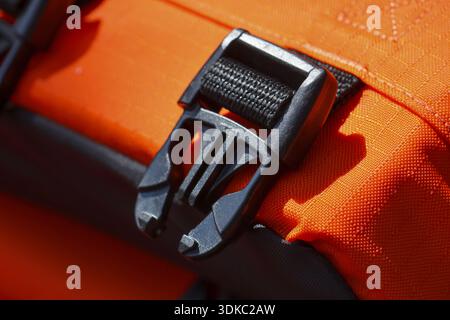 Secure black plastic buckle and clasp on an orange strap. close up detail of outdoor safety equipment with strong fastener, symbol of preparedness for Stock Photo