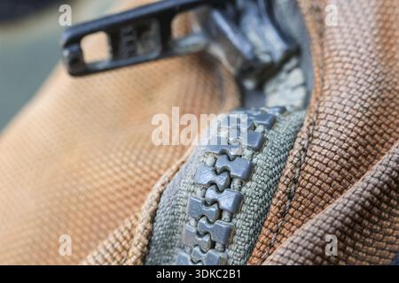 Detailed close up macro shot of grey zipper on brown textured fabric background. view of interlocking teeth of fastener on piece of clothing or bag Stock Photo