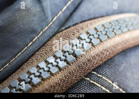 Detailed macro shot of grey zipper on blue fabric, clothing fastener showing sturdy texture of textile, strong seam and an industrial fashion design d Stock Photo
