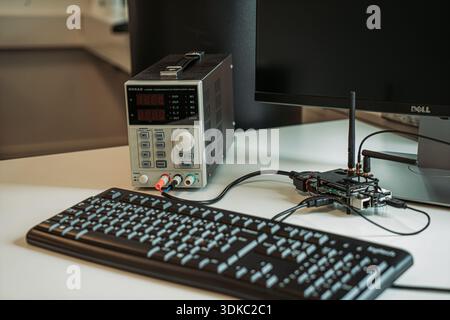 Electronics engineering workspace with a bench power supply, computer keyboard, monitor and a small wireless circuit board with antenna Stock Photo