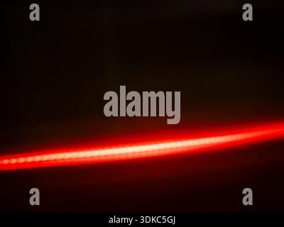 Vibrant red light stream illuminating a dark background, forming a distinct horizontal line composed of many individual points of light, symbolizing c Stock Photo