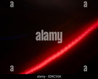 Red light stream creating a dynamic diagonal movement against a dark background, forming an abstract pattern with glowing highlights and subtle lens f Stock Photo
