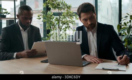 Two diverse multiracial businessmen teamwork in office two men business workers employers discussing online stats result graphics project startup with Stock Photo