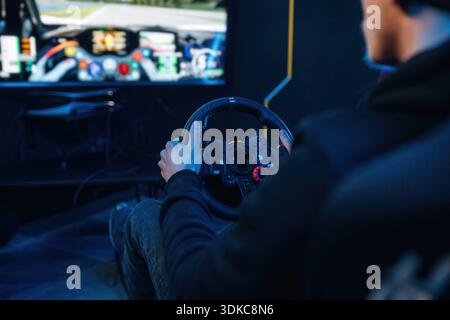 Using steering wheel. Young guy is playing racing game by using driving simulator. Stock Photo