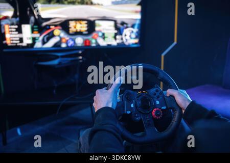 Using steering wheel. Young guy is playing racing game by using driving simulator. Stock Photo
