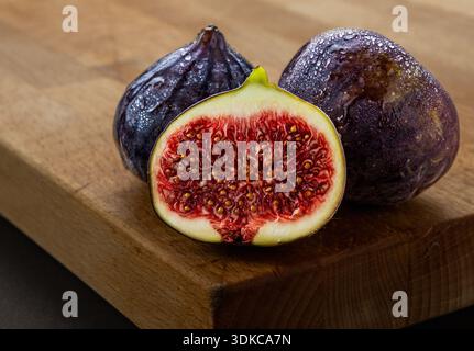 A studio still life of fresh mission figs against a vibrant red background. One whole fig stands prominently in the foreground, while another is halve Stock Photo