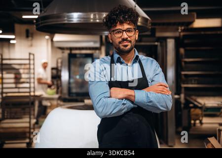 Bakery worker in apron is standing indoors. Stock Photo