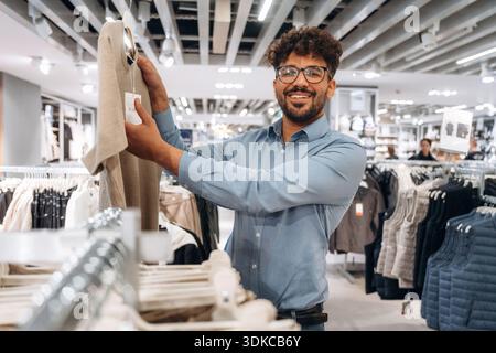 Holding the sweater. Man customer is in the clothing store. Stock Photo