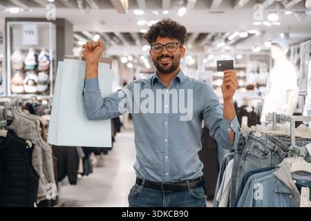 Smiling and holding credit card, shopping. Man customer is in the clothing store. Stock Photo