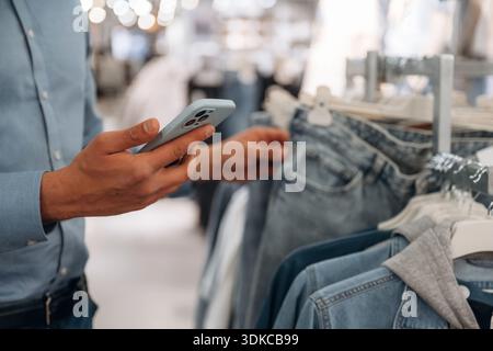 Holding smartphone. Detailed close up view of man that is in clothing store. Stock Photo