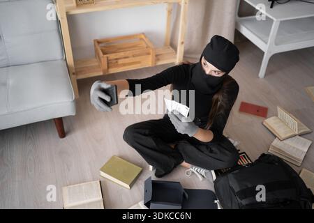 Thief in black balaclava. Female Robber terrorism entering a house for stealing making selfie portrait with money. top view Stock Photo
