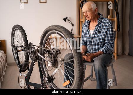 old cyclist sitting near a broken bicycle and thinking about repairs. copy space Stock Photo