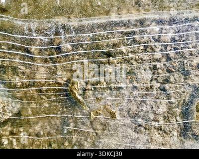 Frozen water surface featuring naturally formed ice lines and delicate crack patterns reveals the rocky bottom. Translucent ice creates unique texture. Stock Photo