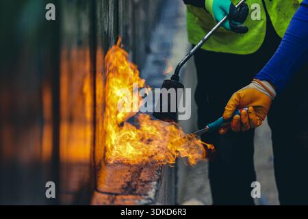Construction workers using a gas torch to apply a bitumen waterproofing membrane during roof installation or repair work Stock Photo
