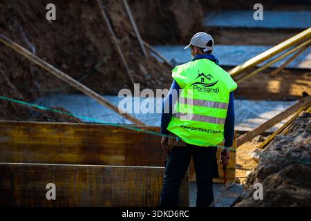 Construction worker holding a hammer while inspecting timber formwork and concrete foundations at an active building site Stock Photo
