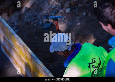 Two construction workers inspecting an excavated foundation area with a hammer and construction materials at an active building site Stock Photo