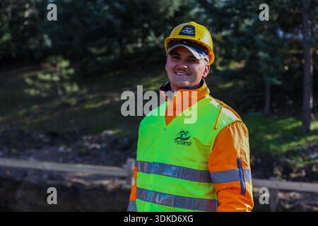 Smiling construction worker wearing a yellow safety helmet and high-visibility vest at an outdoor building site Stock Photo
