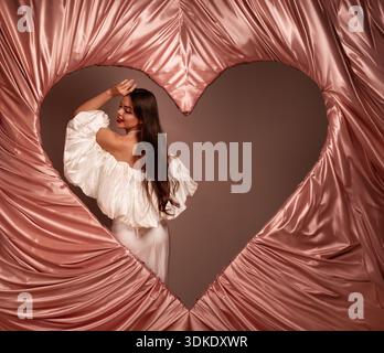 A woman stands gracefully in front of a heart-shaped frame. She embraces the spirit of love for Valentines Day with poise and charm. Stock Photo