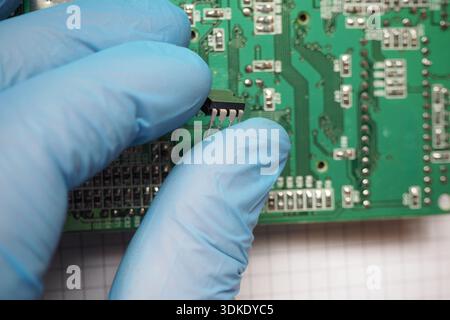 Electronic technician assembles an integrated circuit onto circuit board. Semiconductors in electronics. Stock Photo