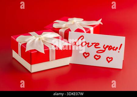 Two Valentine's day gift boxes, white paper card with text Love You on red background. Stock Photo