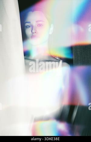 Woman's face seen through shimmering light leaks, creating an ethereal and colorful atmospheric effect Stock Photo