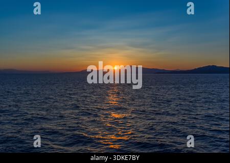 Golden sunset over the Mediterranean Sea with mountain silhouettes and calm water reflections near Greece. Stock Photo
