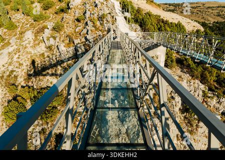 Glass pedestrian bridge on mountain viewpoint with metal structure and rocky landscape under clear sky. Stock Photo