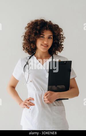 Black notepad is in hand. Beautiful doctor woman is in the studio. Stock Photo