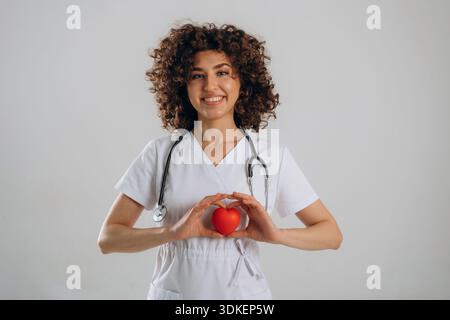 Cardiologist is with little heart toy. Beautiful doctor woman is in the studio. Stock Photo