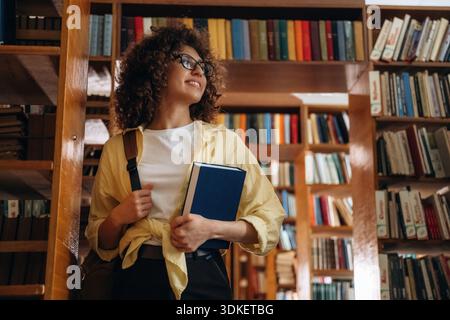 Book in blue hard cover is in hands. Beautiful woman is in the library. Stock Photo