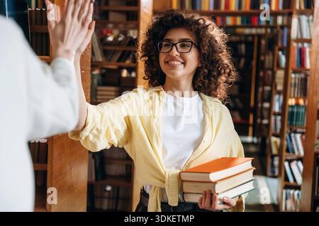 Two women are doing high five in the library. Stock Photo