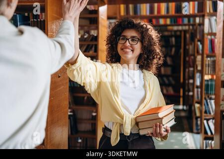 Two women are doing high five in the library. Stock Photo