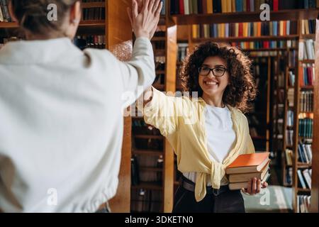 Two women are doing high five in the library. Stock Photo