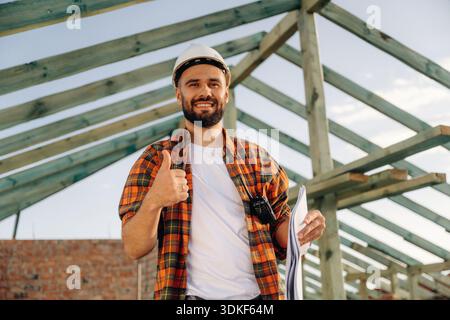 Showing thumb up, smiling. Construction worker is on the roof of a house. Stock Photo