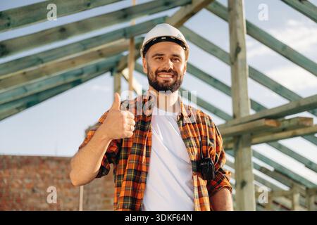 Showing thumb up, smiling. Construction worker is on the roof of a house. Stock Photo