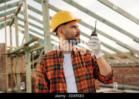 Talking by using walkie talkie. Construction worker is on the roof of a house. Stock Photo