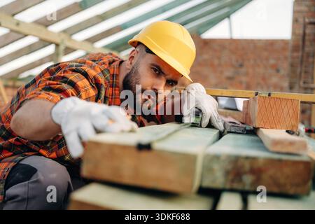 Attention to detail, measuring the plank. Construction worker is on the roof of a house. Stock Photo