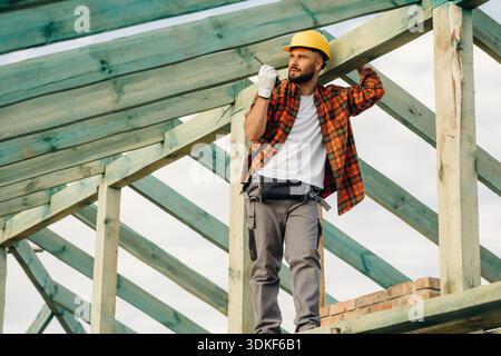 Giving orders by using walkie talkie. Construction worker is on the roof of a house. Stock Photo
